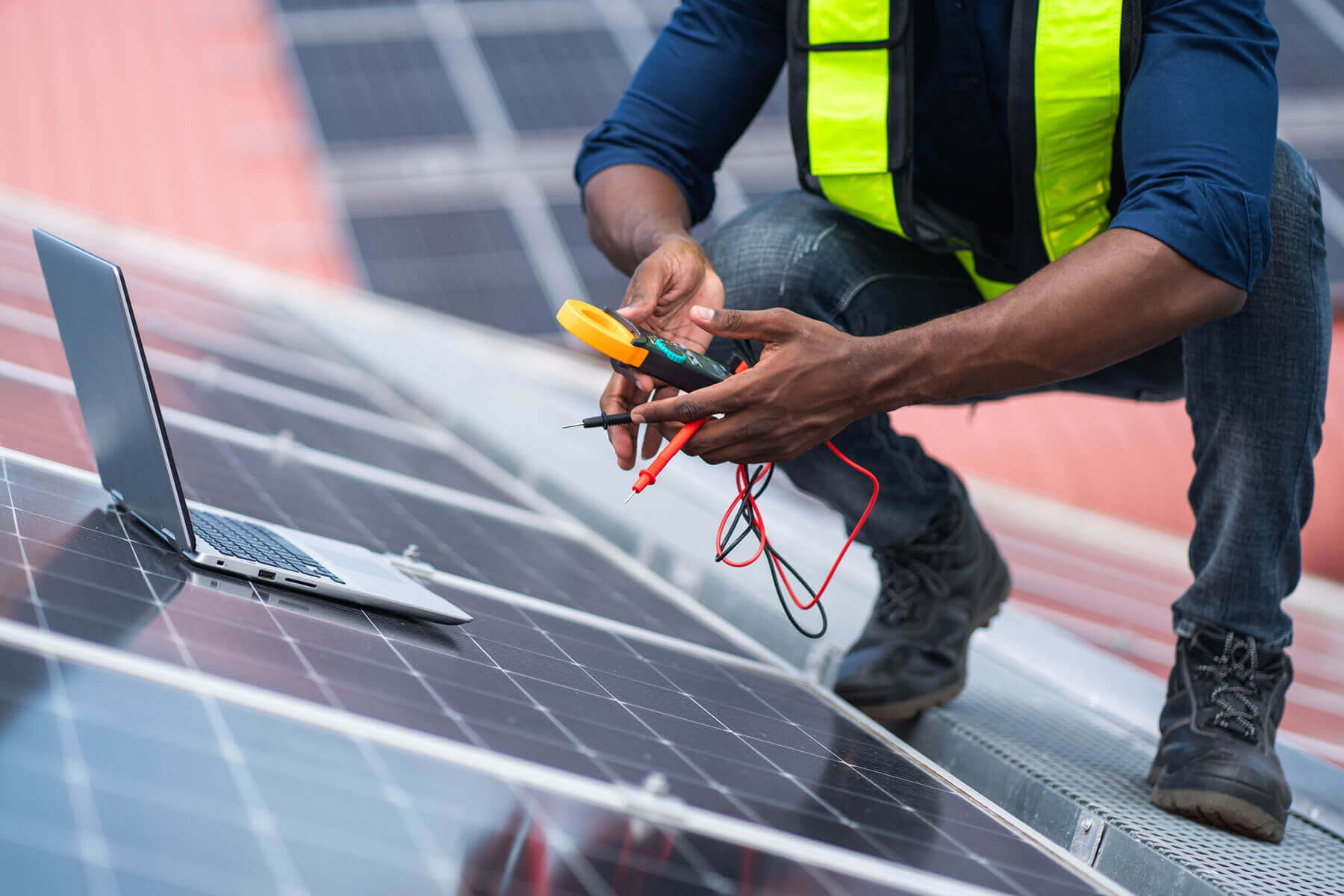 Engineer testing rooftop solar panels with a multimeter and laptop